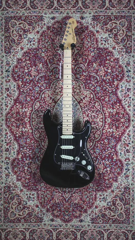 Front view of the Vintage V60 Coaster Series guitar in black, displayed with a rustic backdrop at The Woodshed Guitars shop.