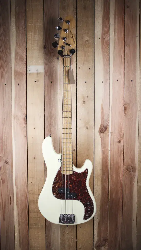 Front view of Sandberg Electra VS 4 Bass in cream, with tortoiseshell pickguard, on a wood panel backdrop.
