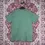 Thumbnail: Back view of sage green Americana tee laid flat on red patterned rug