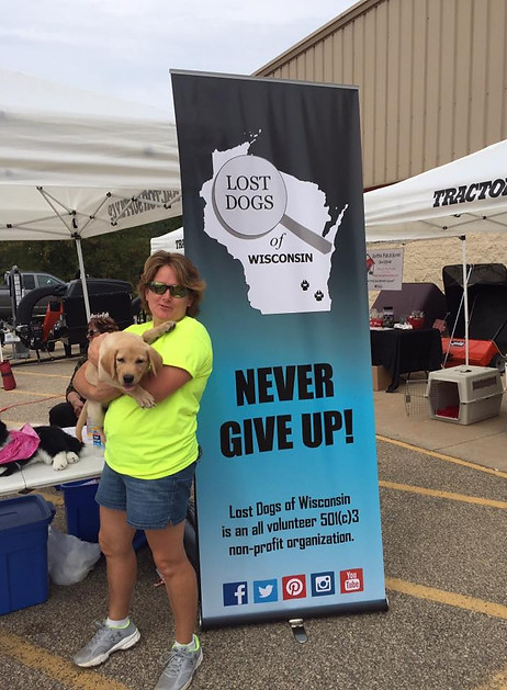 A volunteer holding a puppy next to a Lost Dogs of Wisconsin banner.