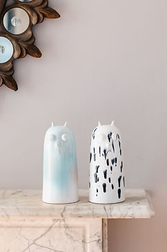 2 identical ornamnets of an animals face, one is white with patches of pale blue and the other is white with black markings