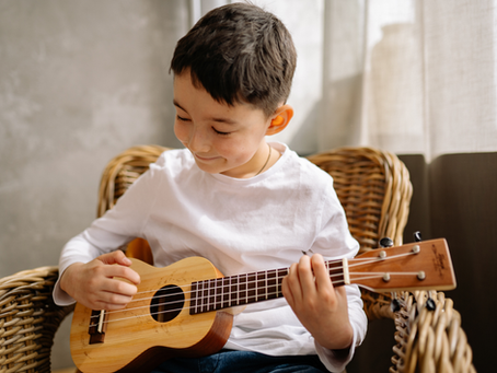 A young boy smiling while playing the ukulele.