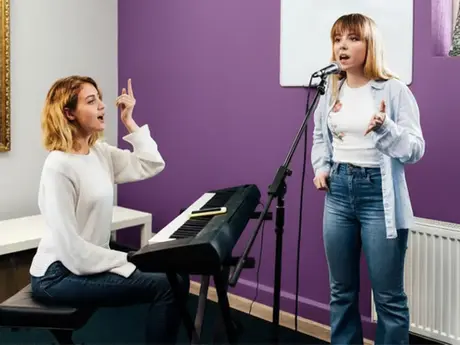 A teenage girl singing as guided by her vocal coach.
