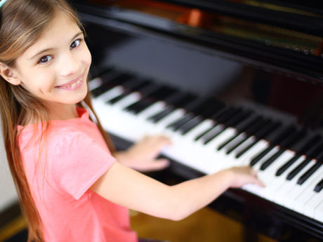 A girl smiling while practicing at the piano.
