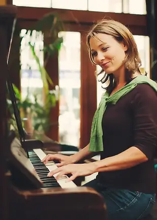 An adult smiling as she plays the piano