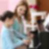 A girl taking piano lesson with her piano teacher sitting next to her.