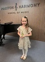 A young girl smiling and holding a trophy that she won from festival participation