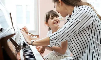A child smiling at her piano teacher as they sit togetherat the piano
