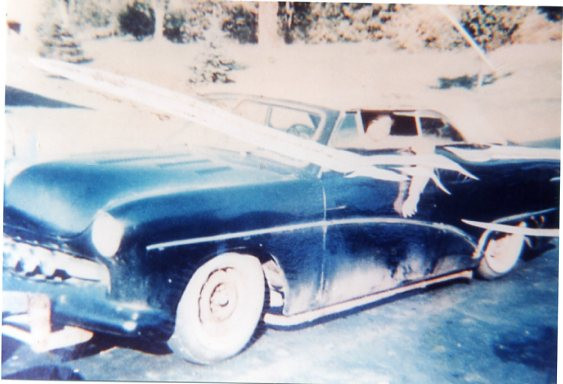 a worn photo of a vintage ford, the paint worn in some places. because of the quality of the photo, the driver is too washed out to see, but his arm hangs out of the window proudly