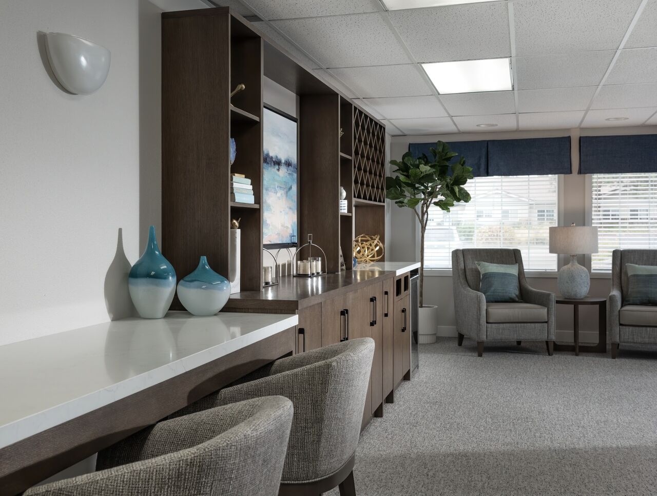 Modern bar area with seating, decor, and large windows with blue shades.