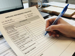 A hand completing a performance review form writing question marks instead of ratings in some sections.