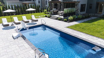 In-ground pool and paver patio in Saratoga Springs, NY with lounge chairs, umbrellas, outdoor kitchen, and landscaped backyard.
