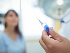 mão de médico com injeção , ao fundo desfocada uma engermeira auxiliar