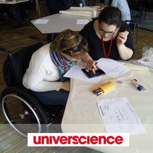 Deux personnes regardent un téléphone portable, assises à une table de travail.