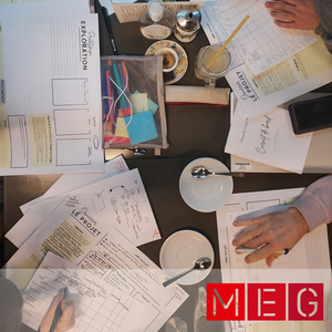 Photo vue du dessus : table couverte de fiches projets, carnet de bord, tasses de jus de gingembre chaud.