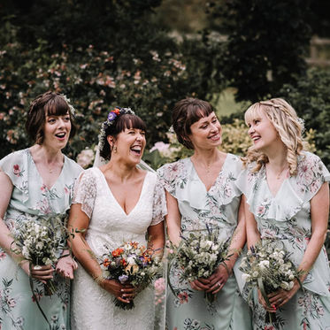 Bride and bridesmaids laugh, floral dresses. Boho styled hair