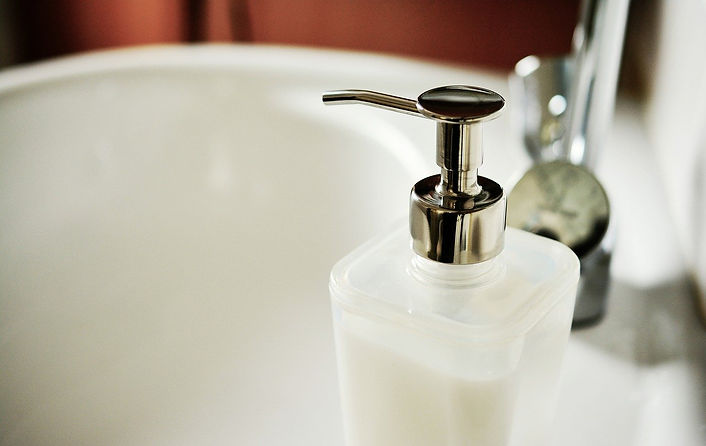 A white soap dispenser with a silver cap. on a white bathroom sink