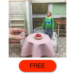 Hand placing miniature cake on table in kitchen with figure, FREE displayed.