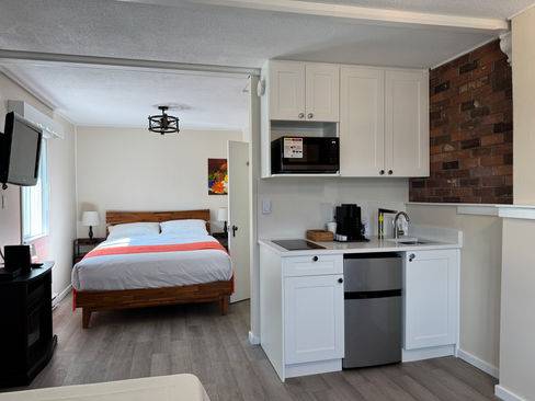 A bright and cozy studio featuring a comfortable bed, a compact kitchenette, and a clean, modern layout.