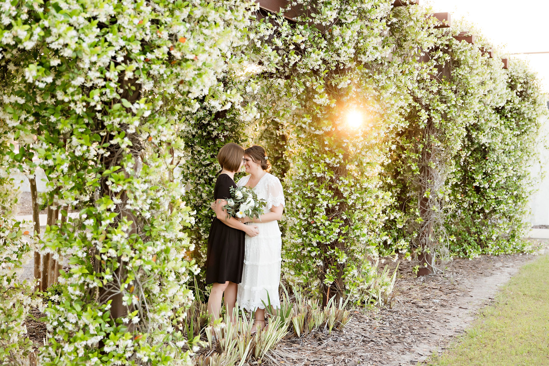 Two brides embracing under a greenery arch