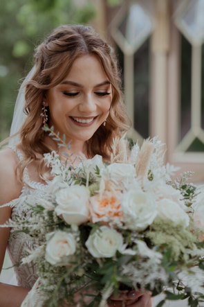 A close up image of a bride smiling while looking at her bouquet
