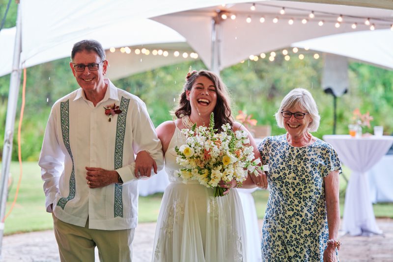 Bride laughing while walking down the isle with her parents on either side of her arms