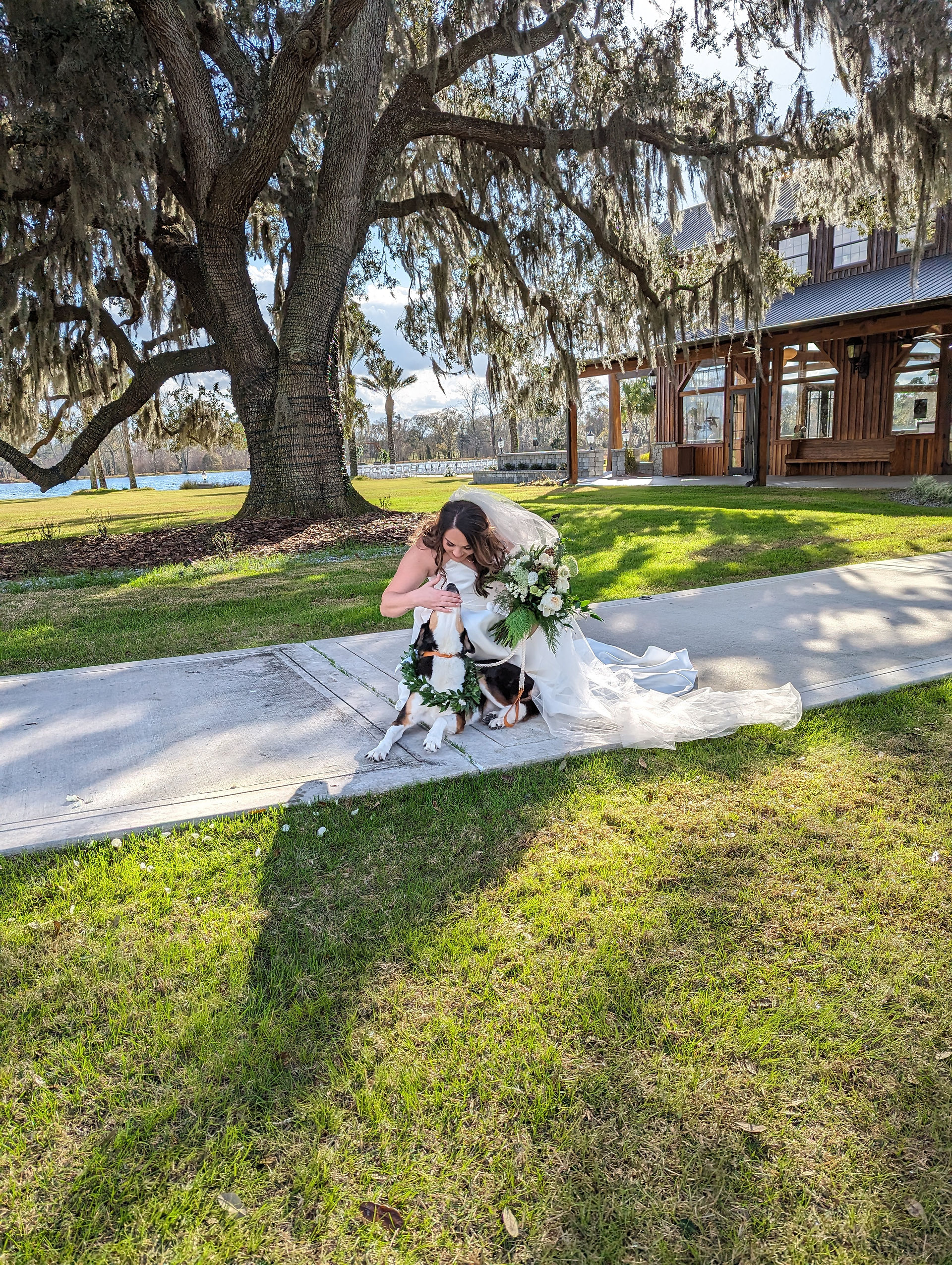 A bride smiling crouched down next to her dog
