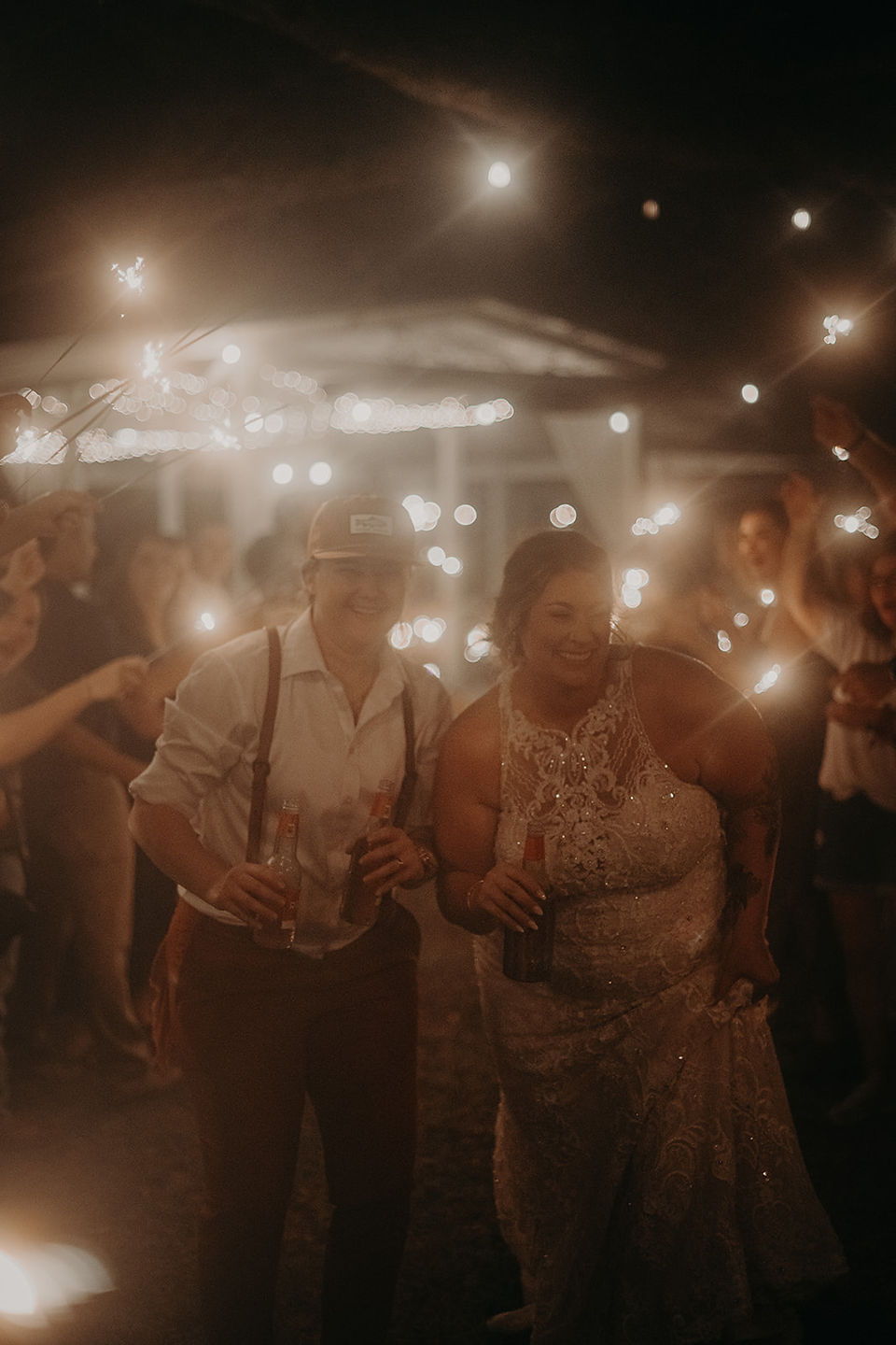 Two brides smiling while walking through a sparkler exit