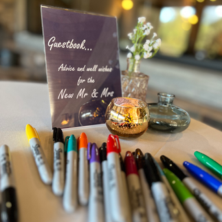 A sign for a wedding guest book with a pile of colored markers in front of it
