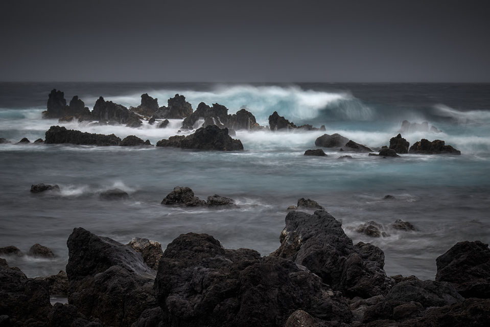 A long exposure of the surf well offshore softens the wave action. The cloudy sky and muted colors give it a mystic feel