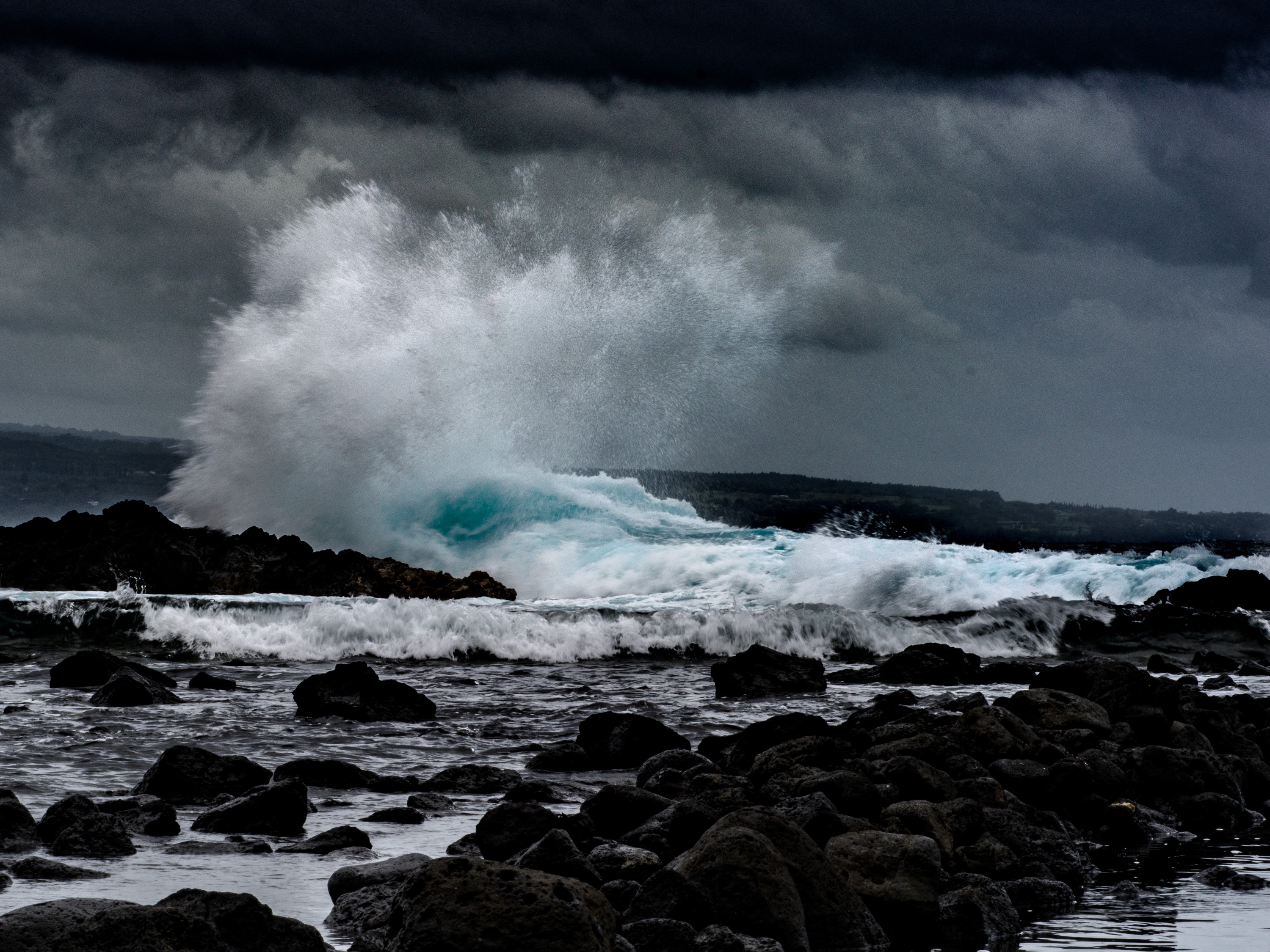 Huge white wave crashes on black lava near a beach