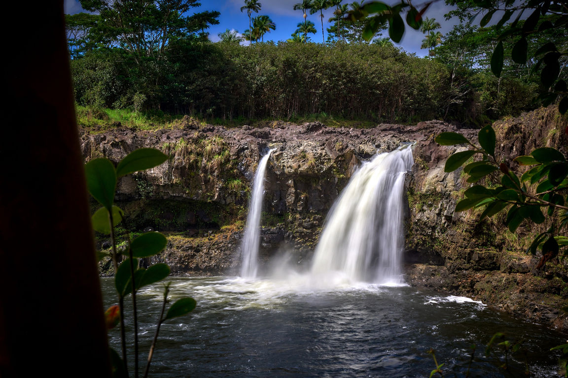 Smooth white falling water falls as multiple streams into a pond at Wailuku Falls
