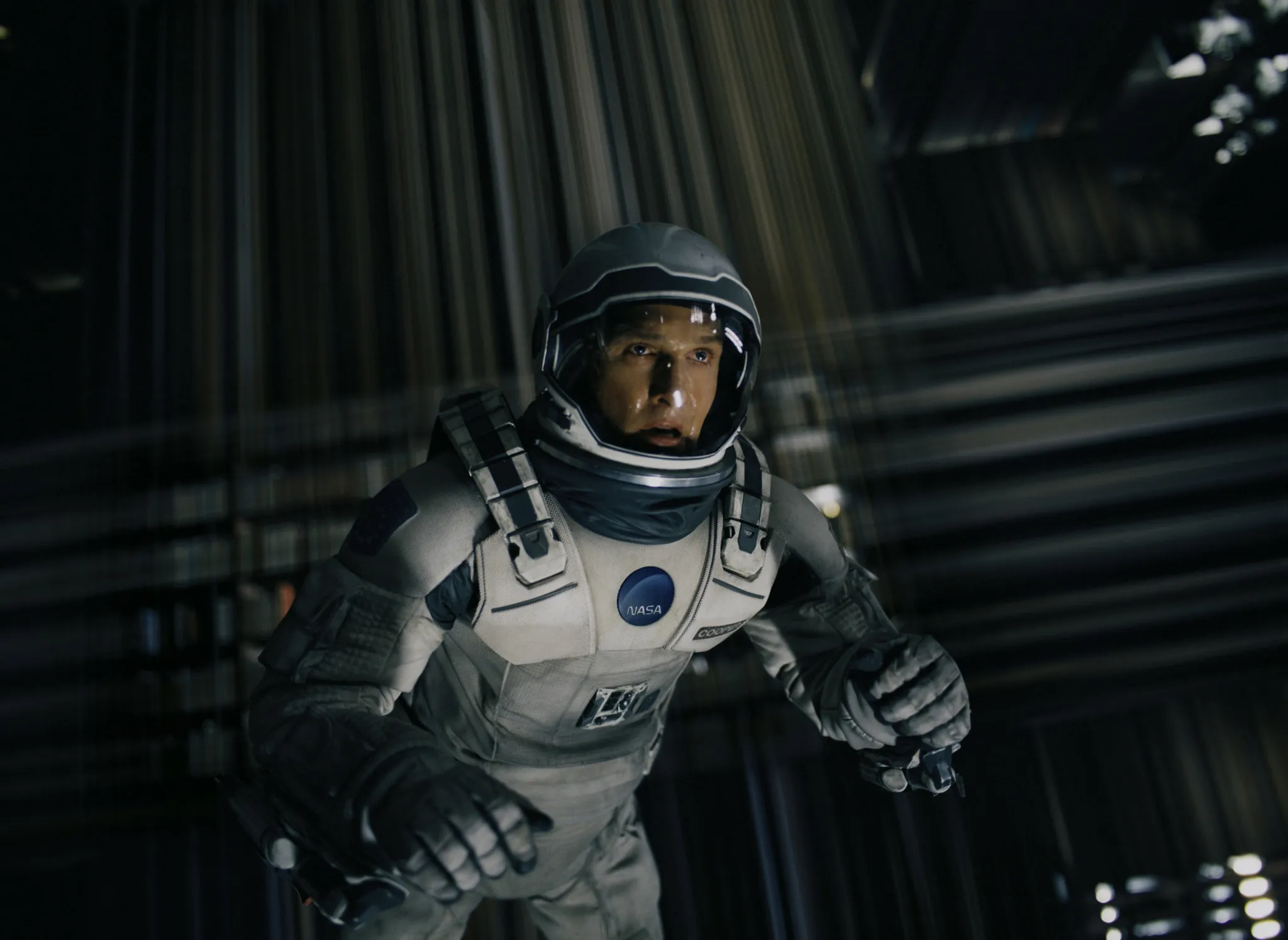 Astronaut in a NASA suit floats/falls through a dark shaft, eyes wide with urgency, on a tense sci-fi mission