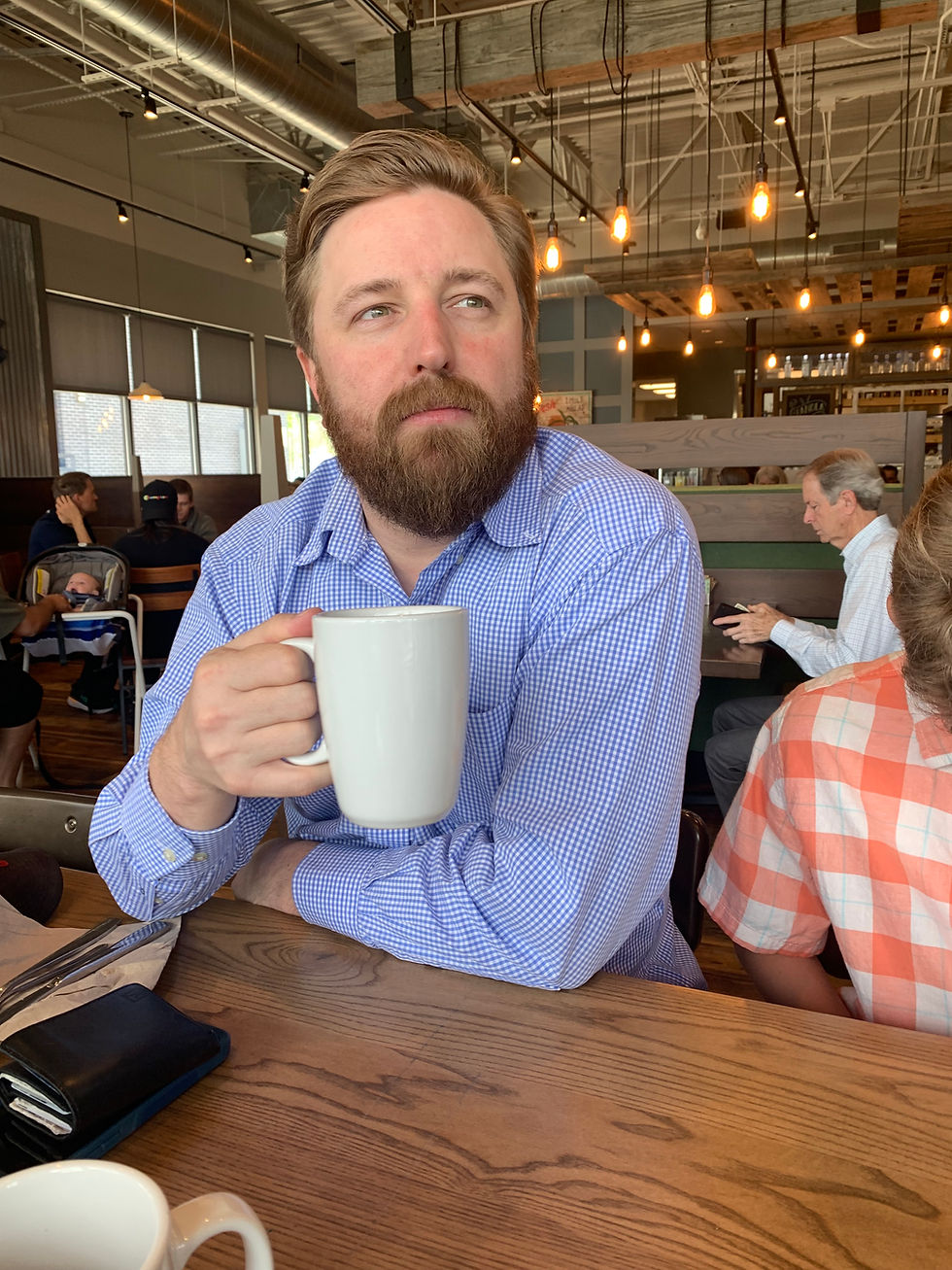 A man holding a white coffee mug with blond hair and wearing a blue checkered shirt