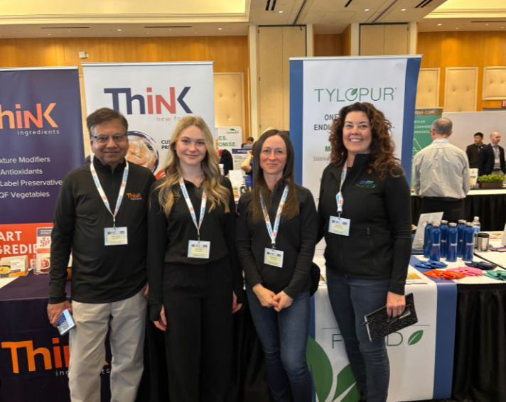 Four people stand together in front of Think and Tylopur booths.