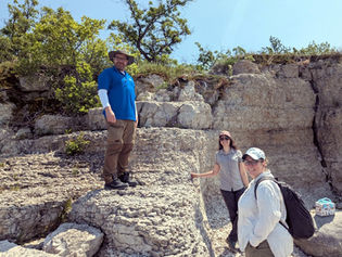 Three scientists stand on a beige rock outcrop smiling for the camera