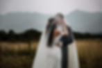 Bride and groom kissing in a scenic field with mountains in the background during their romantic wedding celebration.