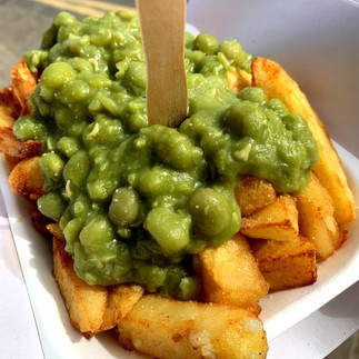 Chips and mushy peas served in a paper tray with a wooden fork