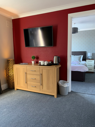 Lounge in deluxe suite at The Headlands Hotel with sofa, TV, and open bedroom door