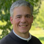 A priest in a green cassock smiling