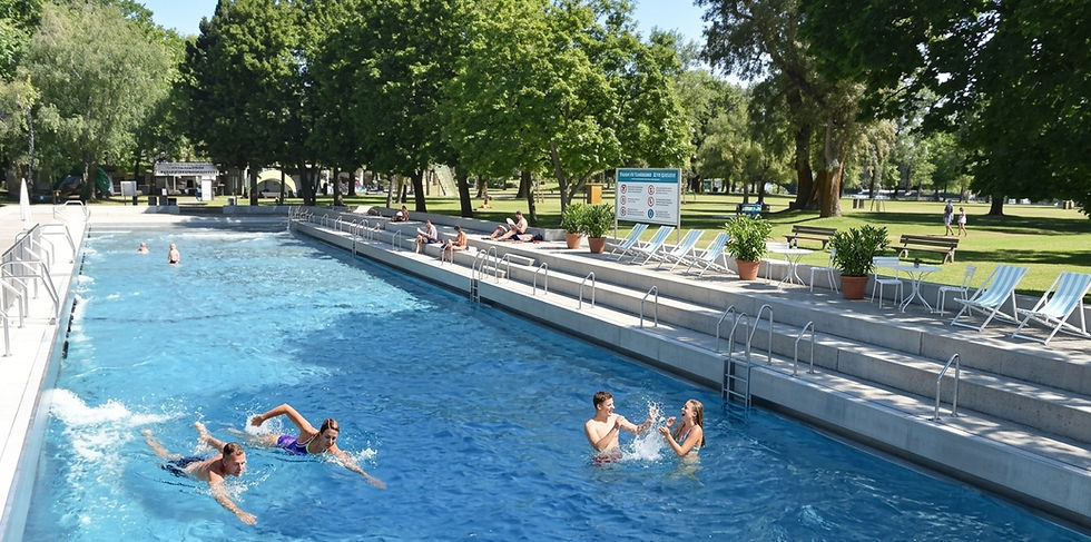 Badegäste im Freibad Schönbrunn mit langgezogenem Pool, Liegestühlen und altem Baumbestand im Sommer