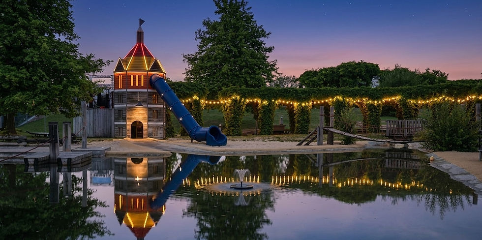 Beleuchteter Kinderspielplatz mit Rutsche und Teich bei Abenddämmerung mit Lichterketten