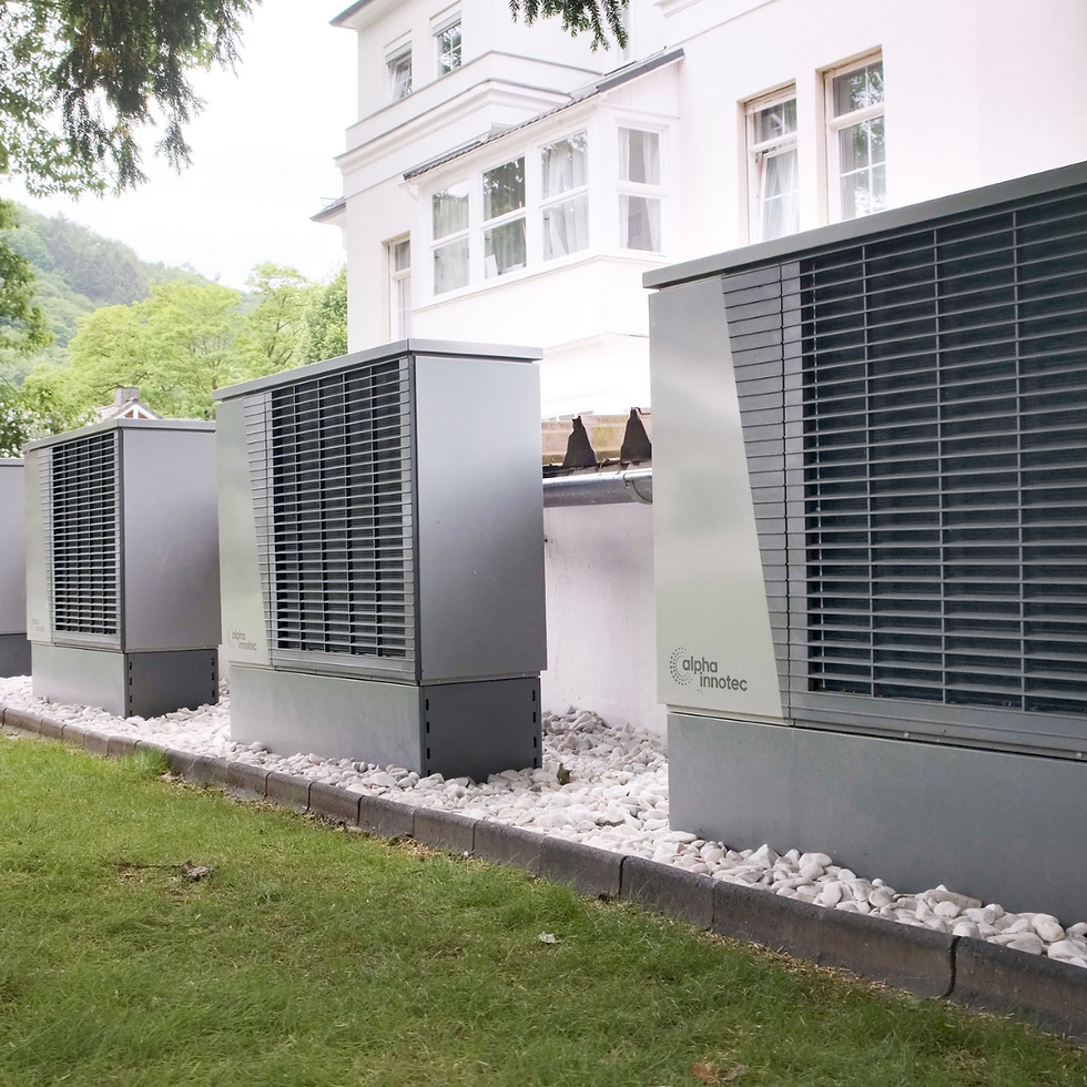 Drei Alpha Innotec Luft-Wasser-Wärmepumpen nebeneinander vor einer weißen Villa, auf Kiesbett aufgestellt