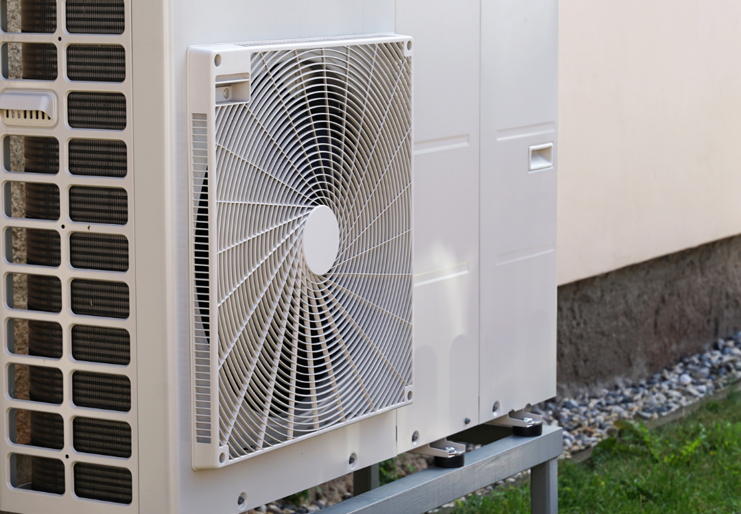 Außeneinheit einer Wärmepumpe mit sichtbarem Ventilator, montiert auf Metallgestell an einer Hauswand