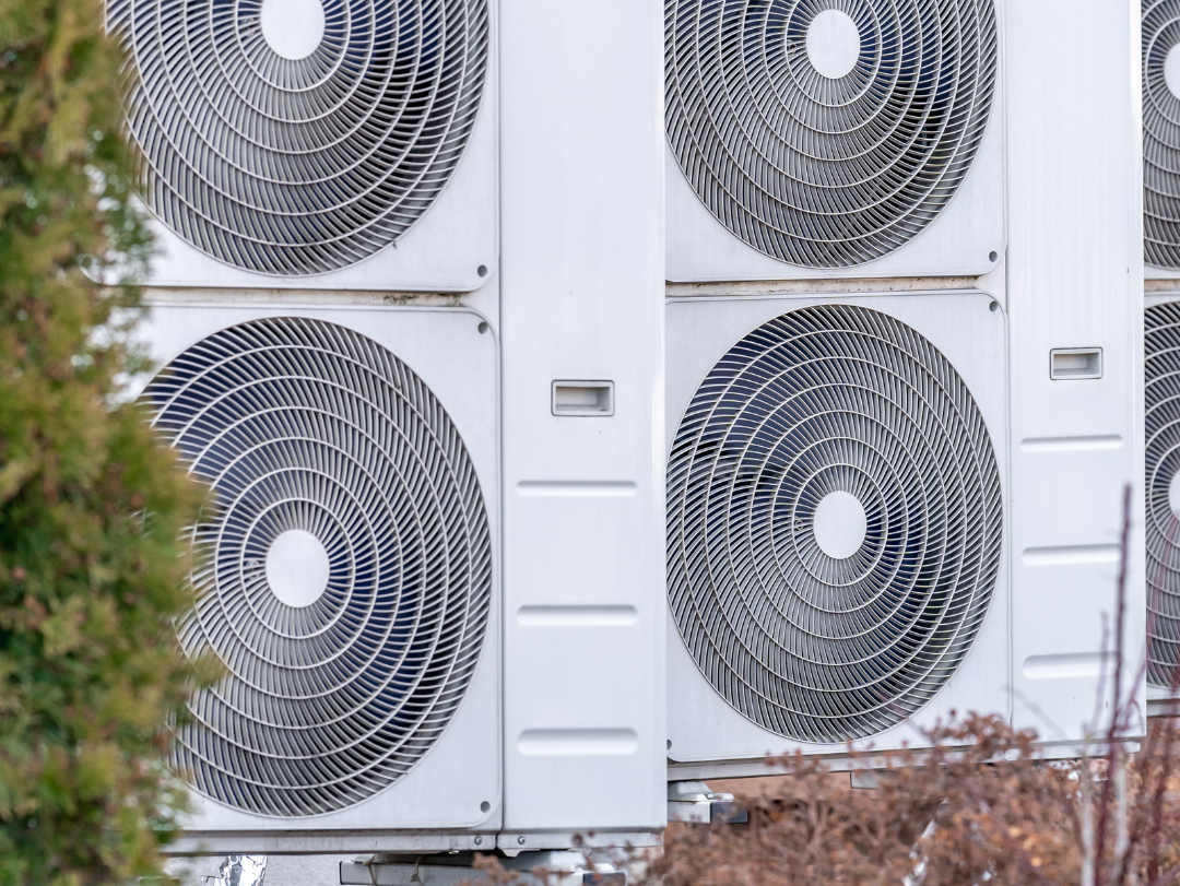 Mehrere Außeneinheiten von Wärmepumpen mit je zwei großen Ventilatoren, aufgestellt vor einem Gebäude