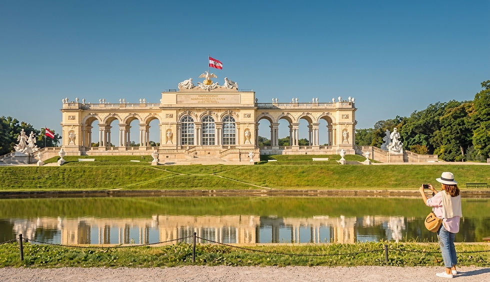 Touristin fotografiert die Gloriette im Schlosspark Schönbrunn, Wien, bei blauem Himmel mit Spiegelung im Teich