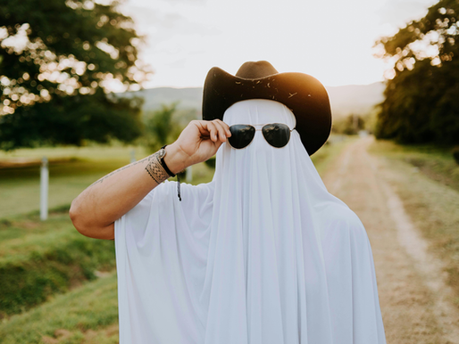 Man in ghost costume with cowboy hand and sunglasses on a road at sunset