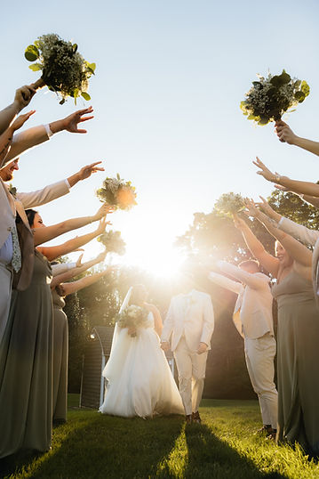 a bride and groom walking through a tunnel of thier bridal party with the sun bright in the background at Stevenson Ridge in Spotsylvania Virginia Captured by a Fredericksburg Wedding Photographer.