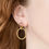 Thumbnail: Close up on womans ear, Ellipse double circle drop earrings with shimmery texture in Gold
