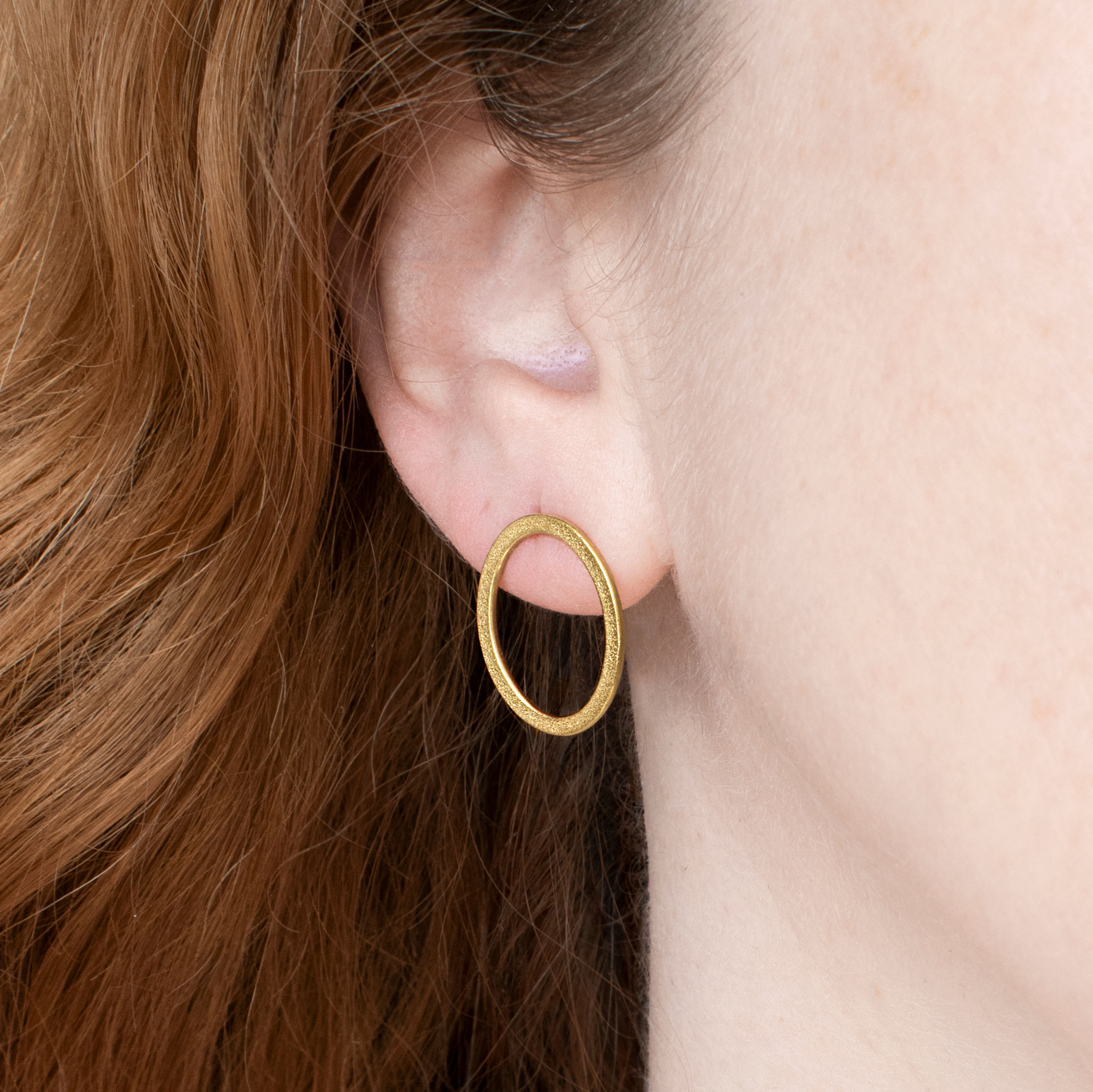 Ellipse small textured oval wire stud earrings in gold, close up on ear